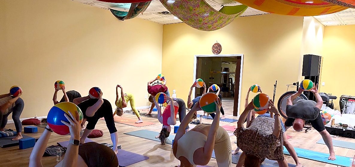 The main room at Buddha Jams during class, with yellow walls, a wood floor and a stage at the far end